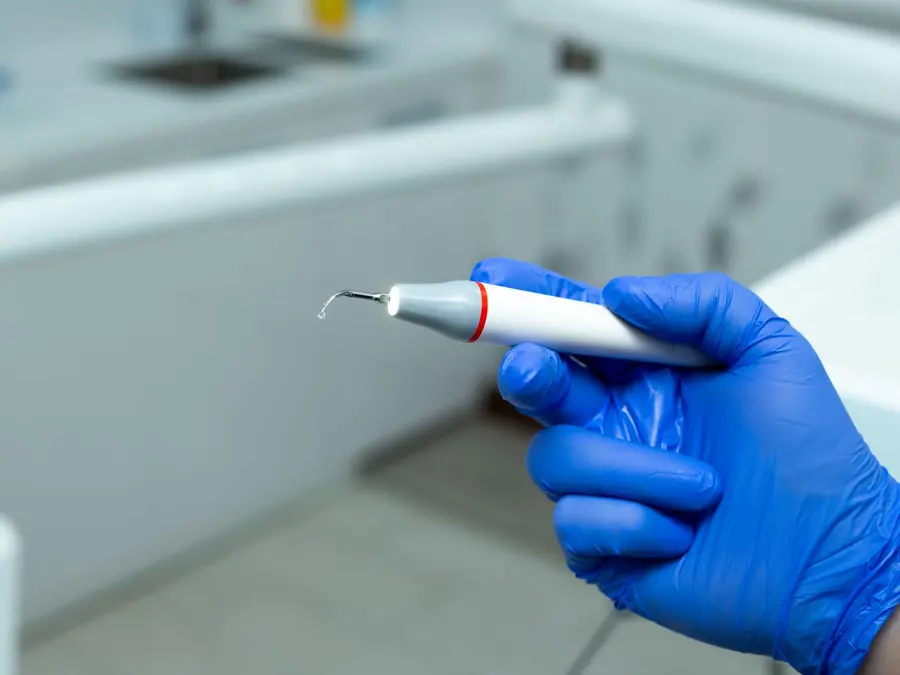 An ultrasonic scaler tip held in a gloved hand, with a drop of water at the tip