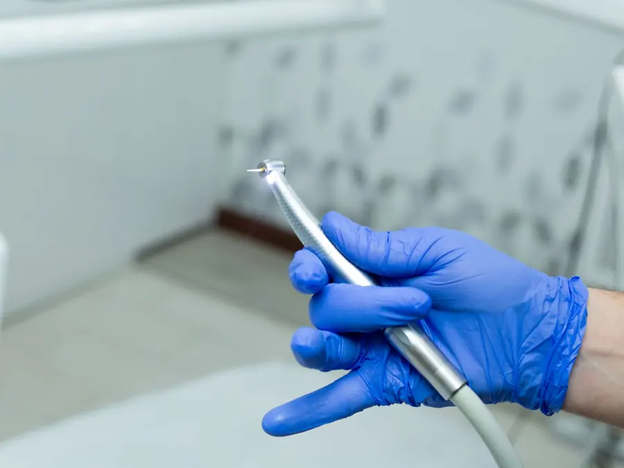 A dental handpiece held in a gloved hand in a treatment room
