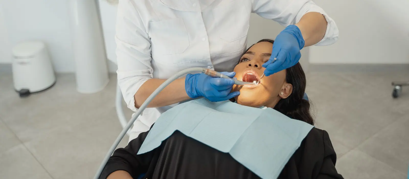 A dentist cleaning a patient's teeth with an ultrasonic scaler and suction